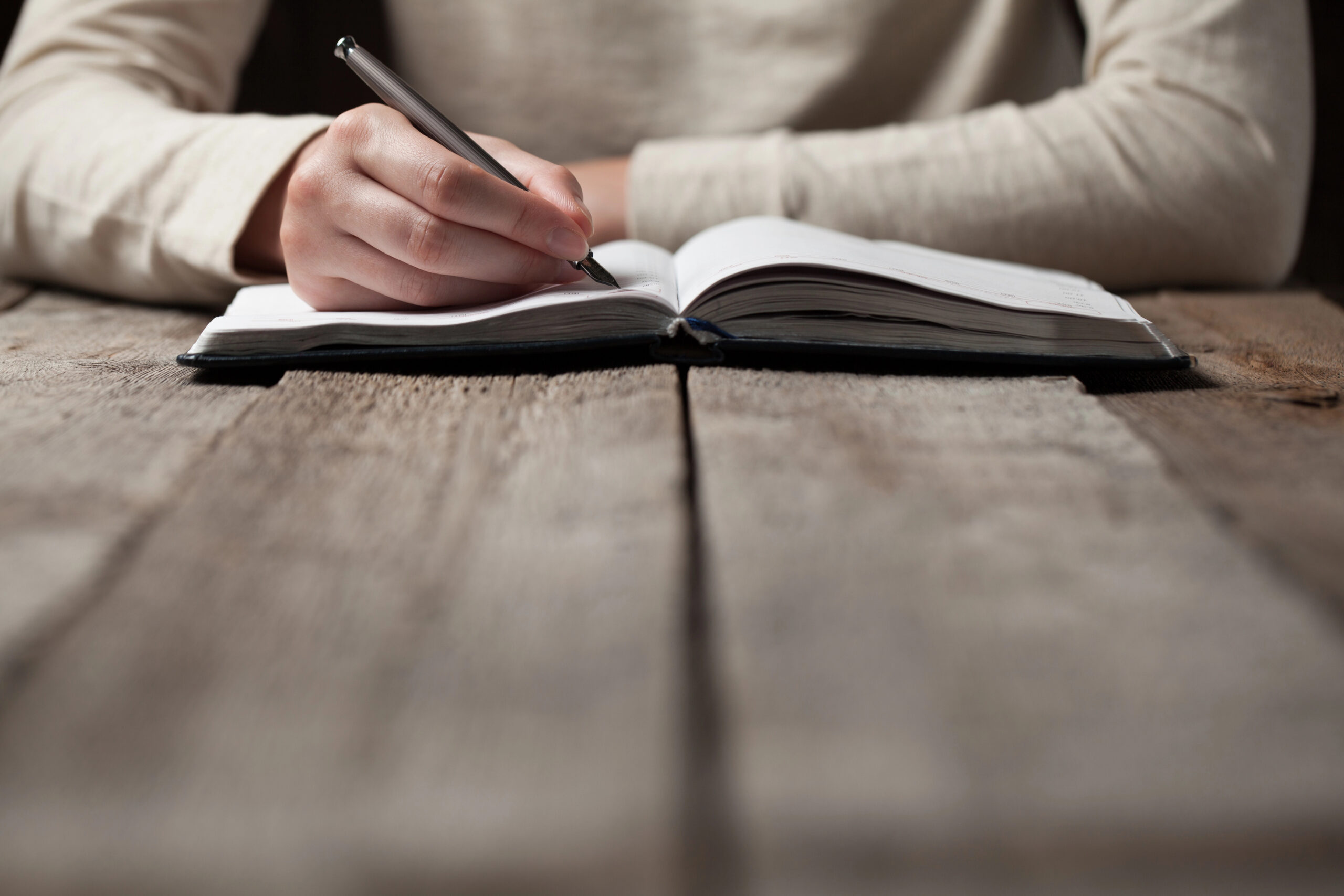 A person writing in a book, sitting at a table.